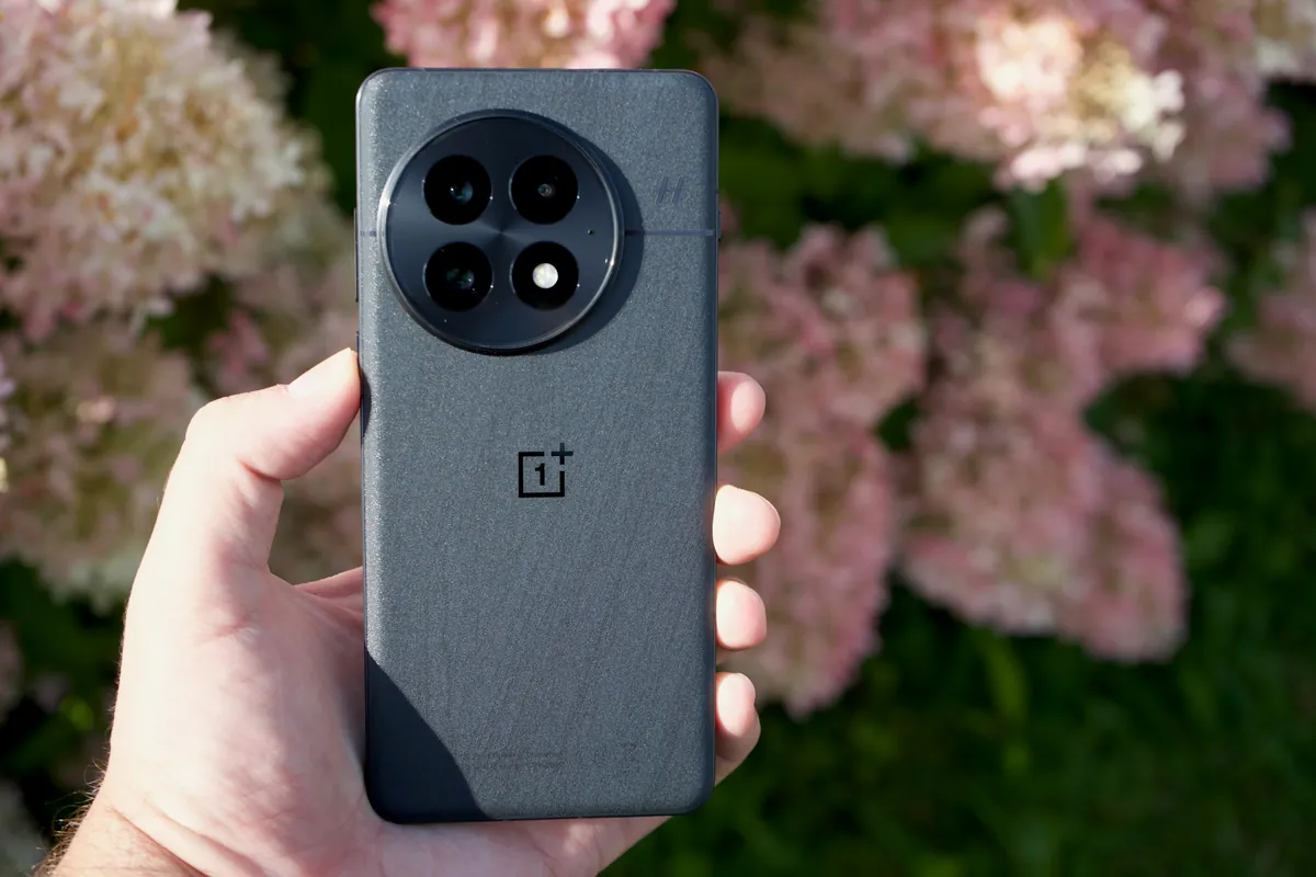 OnePlus 13 in a dark textured finish, back view with its round camera module, held in hand