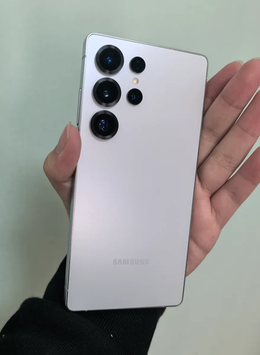 Samsung Galaxy S25 Ultra in a light silver finish, back view showing the camera array, held in hand