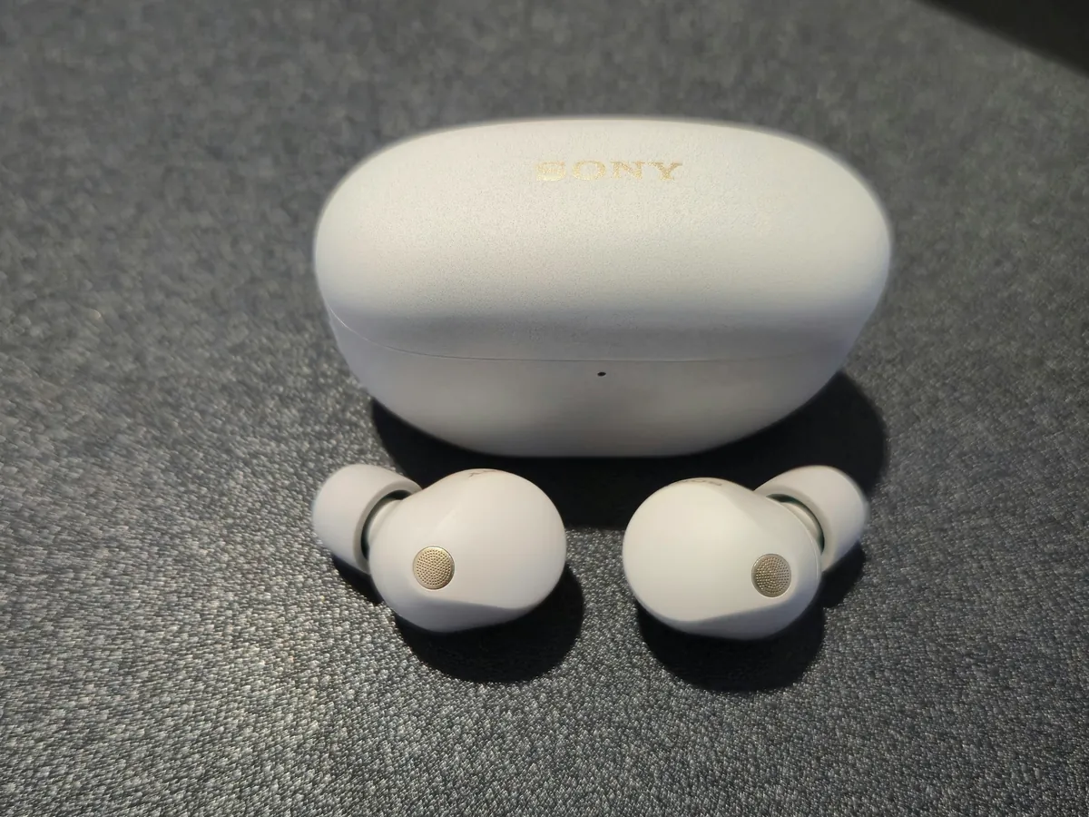Sony WF-1000XM5 earbuds and charging case in Platinum Silver on a dark textured surface